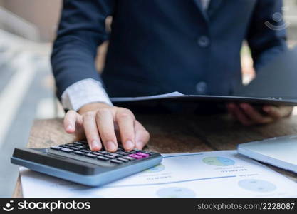 Businessman concept the male accountant using the calculator to check the correctness of the numerical data in the info chart on the wooden table.