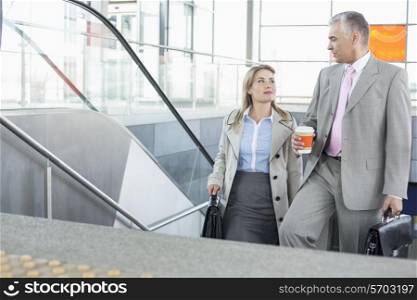 Businessman conversing with female colleague while walking up stairs in train station