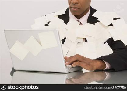 Businessman covered with adhesive notes and working on a laptop