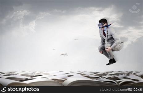 Businessman diver. Young businessman in suit and diving mask jumping in pile of books