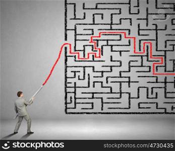 Businessman drawing maze. Young businessman drawing maze on wall with huge pencil