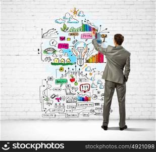 Businessman drawing sketches on wall. Back view image of businessman drawing sketches on wall