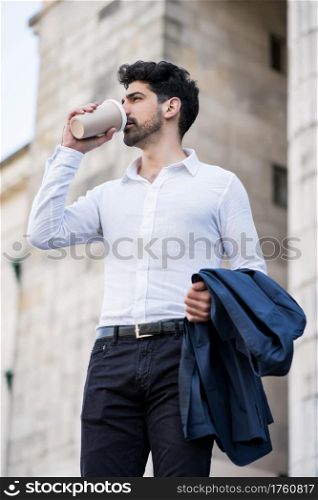 Businessman drinking a cup of coffee on his way to work outdoors on the street. Business concept.