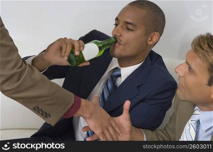 Businessman drinking beer with two businessmen shaking hands beside him