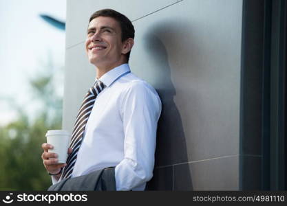 Businessman drinking coffee outdoors. Business man smiling happy holding disposable coffee cup standing near modern building.