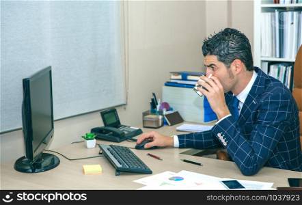 Businessman drinking cup of coffee while working with computer in the office. Businessman drinking coffee and working with computer