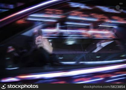 Businessman driving at night, illuminated and reflected lights on the car window
