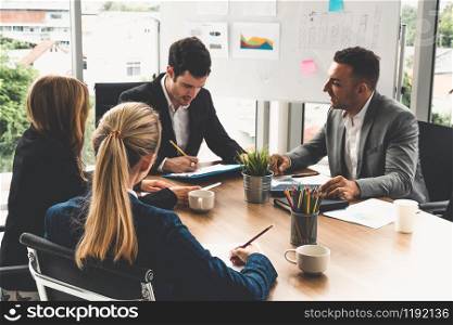 Businessman executive in group meeting discussion with other businessmen and businesswomen in modern office with coffee cups and documents on table. People corporate business working team concept.