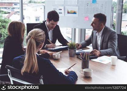 Businessman executive in group meeting discussion with other businessmen and businesswomen in modern office with coffee cups and documents on table. People corporate business working team concept.