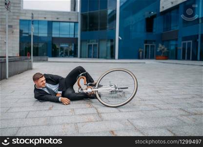 Businessman fell off his bike at the office building in downtown. Business person riding on eco transport on city street. Businessman fell off his bike at office building