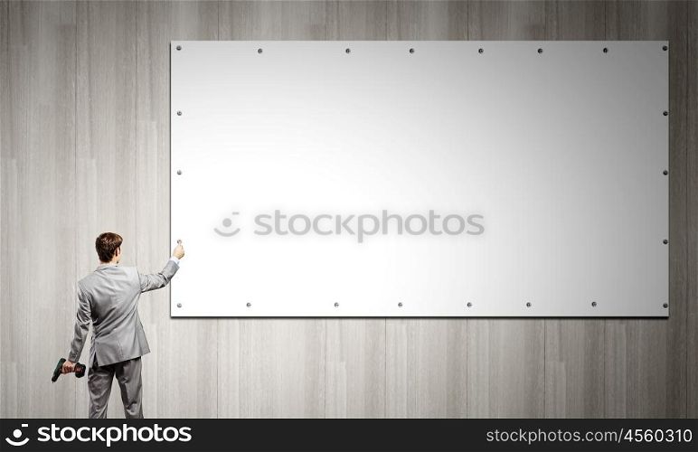 Businessman fixing banner. Rear view of businessman fixing blank white banner on wall