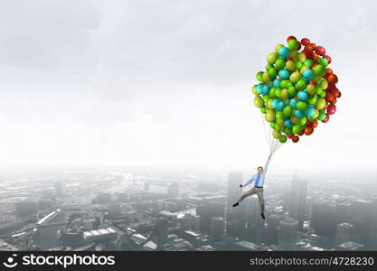 Businessman flies in sky. Young successful businessman flies on bunch of colorful balloons