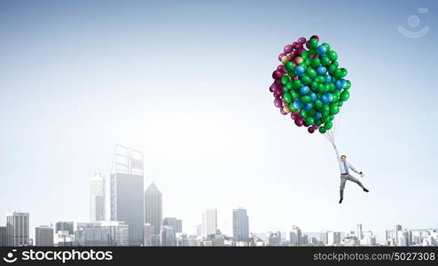 Businessman flies in sky. Young successful businessman flies on bunch of colorful balloons