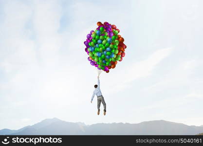 Businessman flies in sky. Young successful businessman flies on bunch of colorful balloons