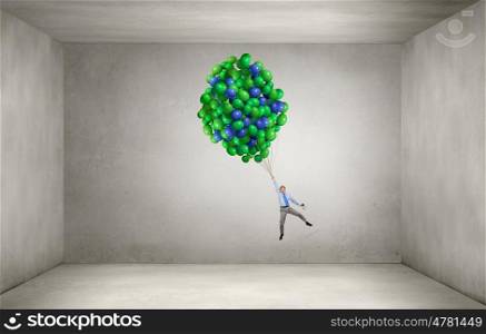 Businessman flying on balloons. Young successful businessman flying on bunch of colorful balloons