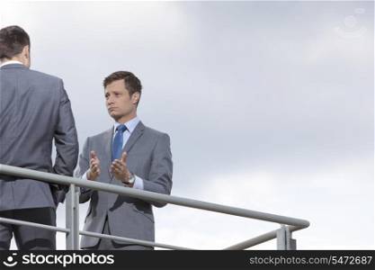 Businessman gesturing while communicating with coworker against sky