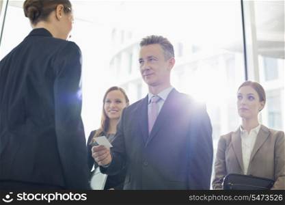 Businessman giving his card to female coworker in office