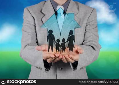 businessman hand holding 3d house with family icon on nature background as insurance concept