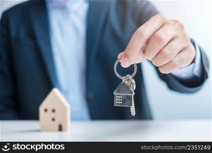 Businessman hand holding key with wooden Home model. Real estate, buy and sale, Property insurance, rental and contract agreement concepts