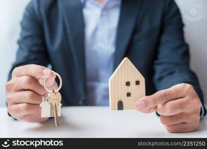 Businessman hand holding key with wooden Home model. Real estate, buy and sale, Property insurance, rental and contract agreement concepts