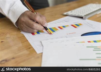 businessman hand holding pen with graph and chart analysis paperwork document on office desk