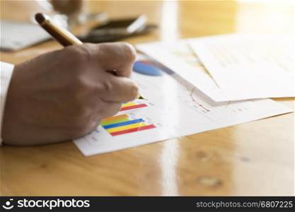 businessman hand holding pen with graph and chart analysis paperwork document on office desk