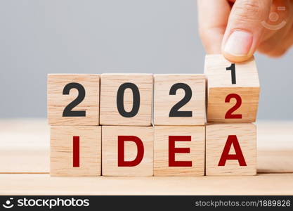 Businessman hand holding wooden cube and flip over block 2021 to 2022 IDEA on table background. Resolution, plan, Trend, change, start and New Year holiday concepts