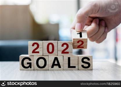 Businessman hand holding wooden cube with flip over block 2021 to 2022 GOALS word on table background. Resolution, strategy, solution, goal, business and New Year holiday concepts