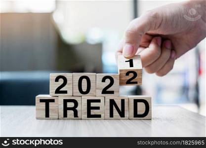Businessman hand holding wooden cube with flip over block 2021 to 2022 TREND word on table background. Resolution, strategy, solution, goal, business and New Year holiday concepts