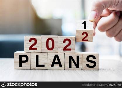 Businessman hand holding wooden cube with flip over block 2021 to 2022 Plans word on table background. Resolution, strategy, solution, goal, business and New Year holiday concepts