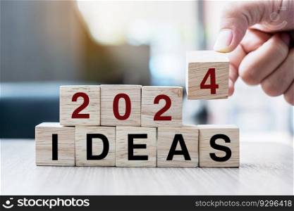 Businessman hand holding wooden cube with flip over block 2023 to 2024 Plans word on table background. Resolution, strategy, solution, goal, business and New Year holiday concepts