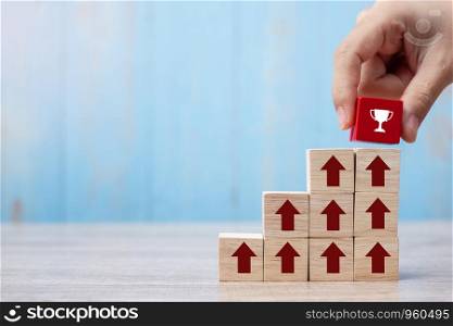 Businessman hand placing or pulling Red block with Trophy and growth up arrow on table background. Business Growth, Improvement, strategy, Successful, success, winner and Mission complete Concepts