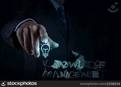 businessman hand pointing  light bulb with design word KNOWLEDGE MANAGEMENT on virtual screen computer as concept