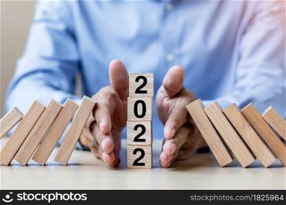Businessman hand Stopping Falling of 2022 wooden Blocks. Business, Risk Management, Insurance, Resolution, strategy, solution, goal, New Year New You and happy holiday concepts