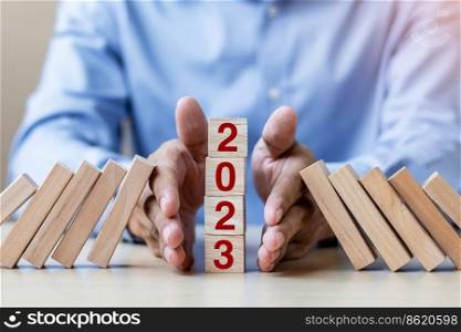 Businessman hand Stopping Falling of 2023 wooden Blocks. Business, Risk Management, Insurance, Resolution, strategy, solution, goal, New Year New You and happy holiday concepts