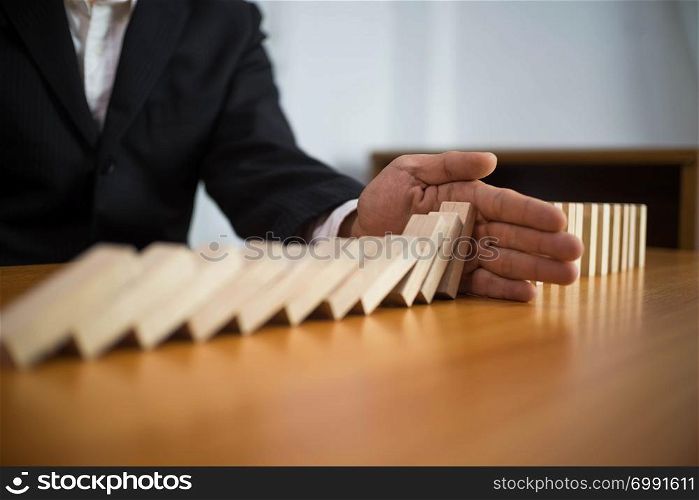 Businessman hand stops domino continuous overturned meaning that hindered business failure. Stop over this business failure concept.