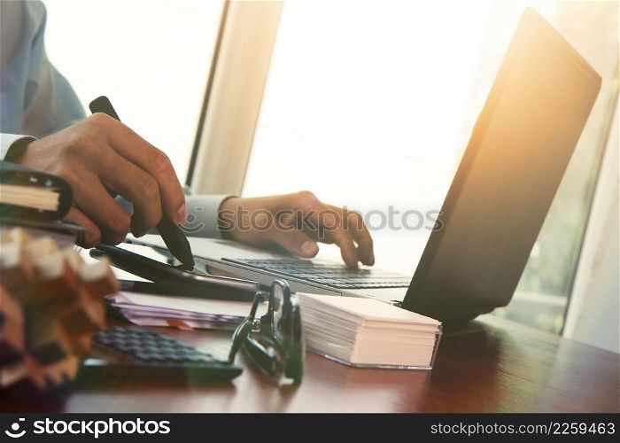 Businessman hand using laptop and mobile phone with overcast effect on wooden desk as concept