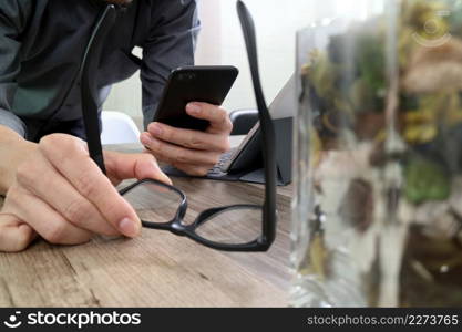 businessman hand with eyeglasses using smart phone,mobile payments online shopping,omni channel,digital tablet docking keyboard computer,flower glass vase on wooden desk