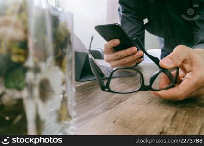 businessman hand with eyeglasses using smart phone,mobile payments online shopping,omni channel,digital tablet docking keyboard computer,flower glass vase on wooden desk,filter