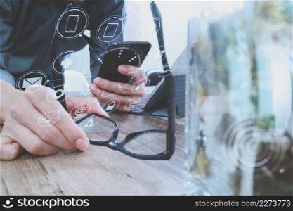 businessman hand with eyeglasses using smart phone,mobile payments online shopping,omni channel,digital tablet docking keyboard computer,flower glass vase on wooden desk,virtual interface icons screen
