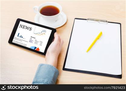 businessman hand with tablet PC with business news on screen at office table