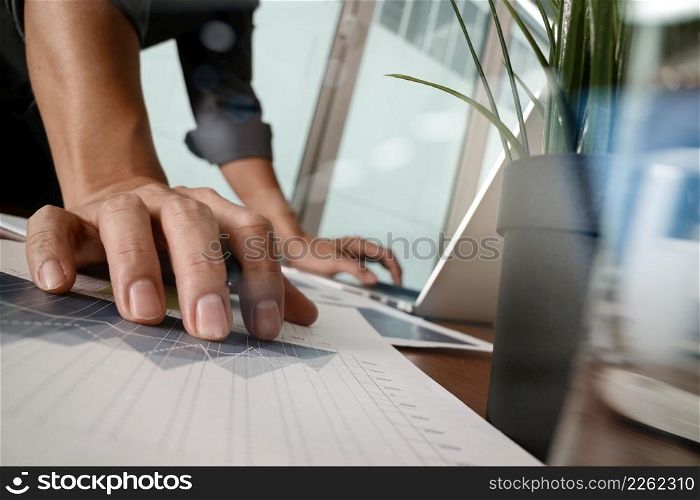 businessman hand working with new modern computer and business strategy documents with glass of water and greenplant foreground on wooden desk in office