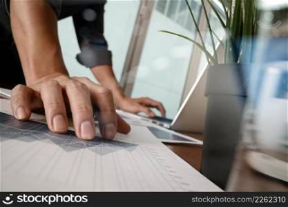 businessman hand working with new modern computer and business strategy documents with glass of water and greenplant foreground on wooden desk in office