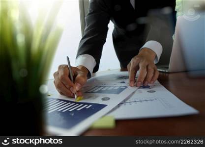 businessman hand working with new modern computer and business strategy documents with green plant foreground on wooden desk in office