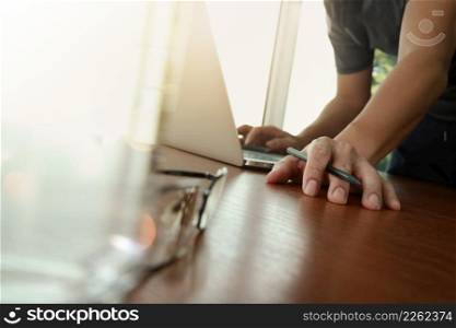 businessman hand working with new modern computer and business strategy documents with green plant and glass of water and eyeglasses foreground on wooden desk in office