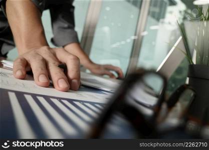 businessman hand working with new modern computer and business strategy documents with green plant and eye glasses foreground on wooden desk in office