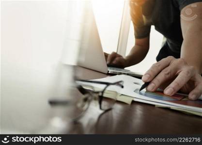 businessman hand working with new modern computer and business strategy documents with glass of water and eye glasses foreground on wooden desk in office