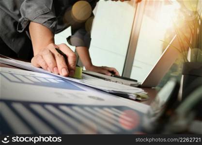 businessman hand working with new modern computer and business strategy documents with green plant and eye glasses foreground on wooden desk in office
