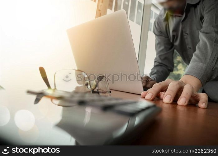 businessman hand working with new modern computer and smart phone and business strategy on wooden desk with calculator and eyeglass foreground as concept