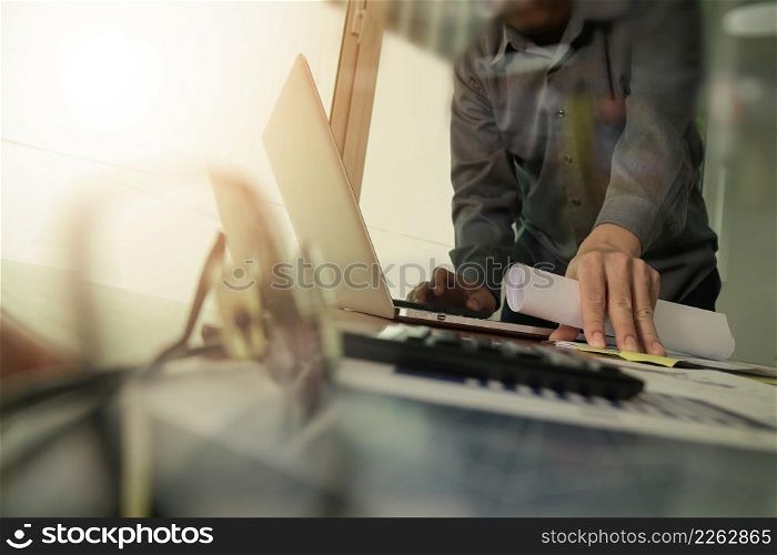 businessman hand working with new modern computer and smart phone and business strategy document on wooden desk with calculator and eyeglass foreground as concept